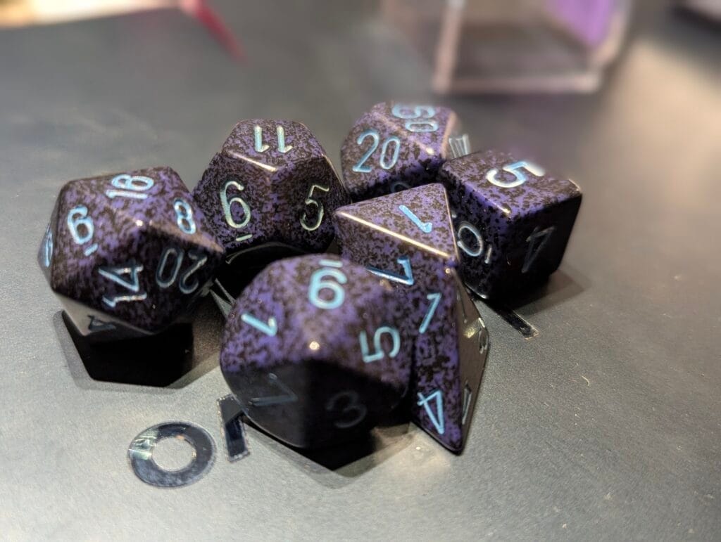 Un set de dés polyhédraux (4, 6, 8, 10, 12 et 20 faces) en couleur "cobalt", un bleu foncé moucheté de bleus plus clairs. Ils reposent sur un ordinateur portable fermé.